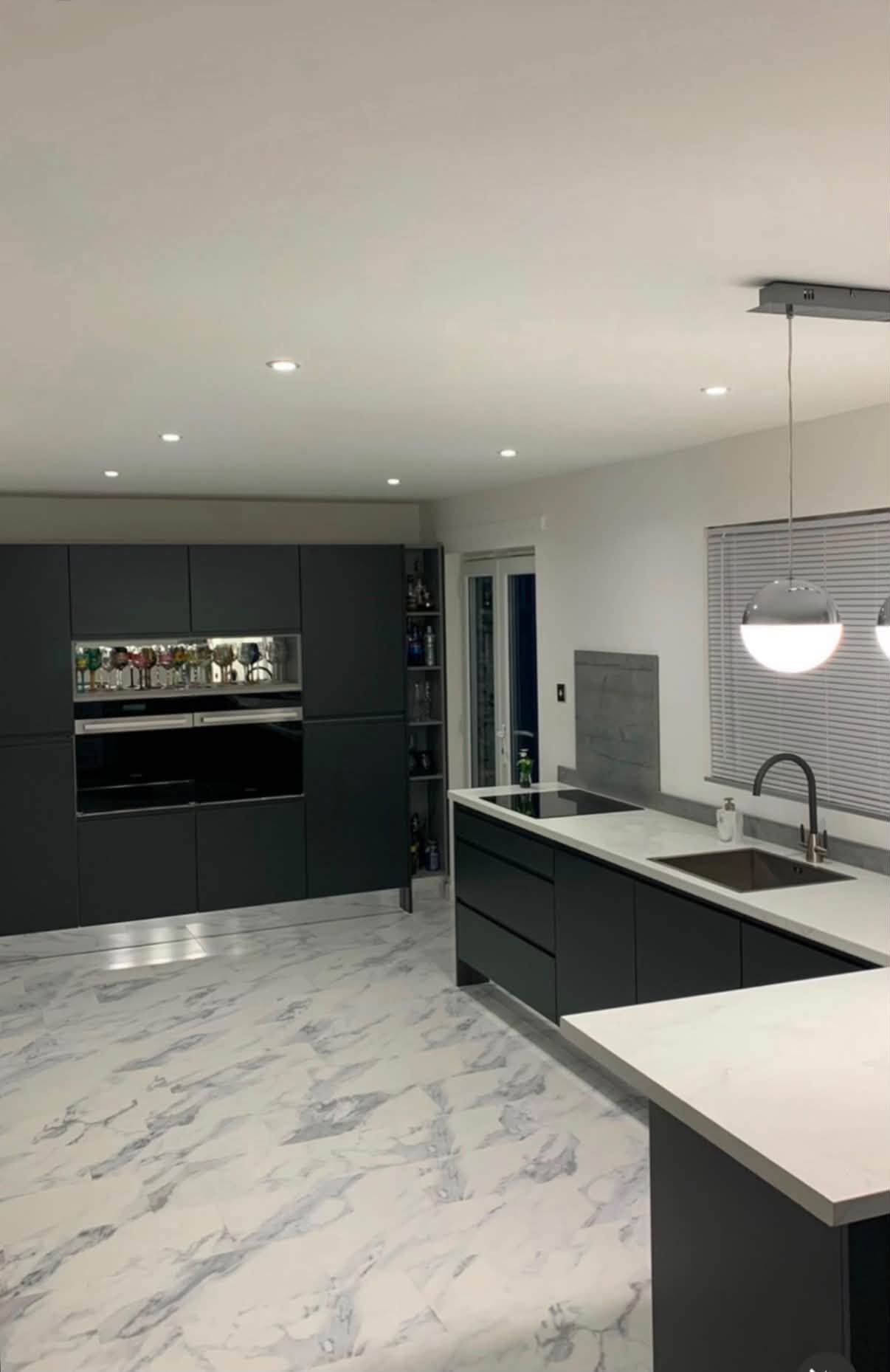 Dark contemporary kitchen installation with a pale stone floor and island
