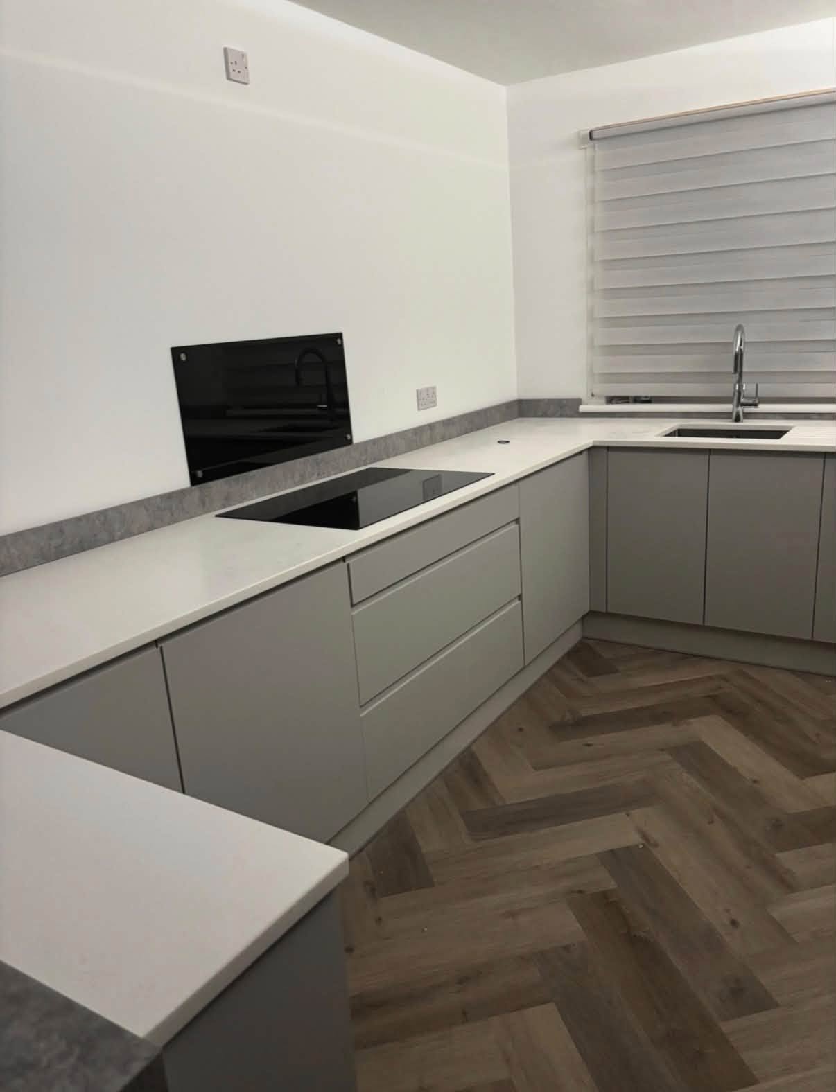Minimal grey fitted kitchen with white worktops and herringbone flooring